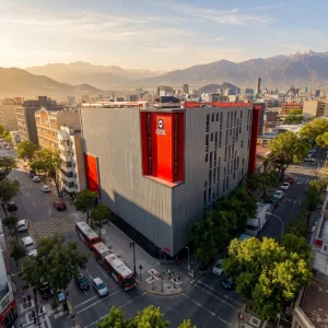 A large grey office building with red vertical banners on a city street, surrounded by trees, with mountains in the distance.