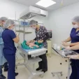 Medical team in scrubs and masks performing a procedure on a newborn infant on a sterile hospital table in a clean operating room.