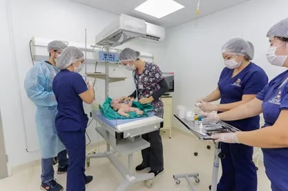 Medical team in scrubs and masks performing a procedure on a newborn infant on a sterile hospital table in a clean operating room.