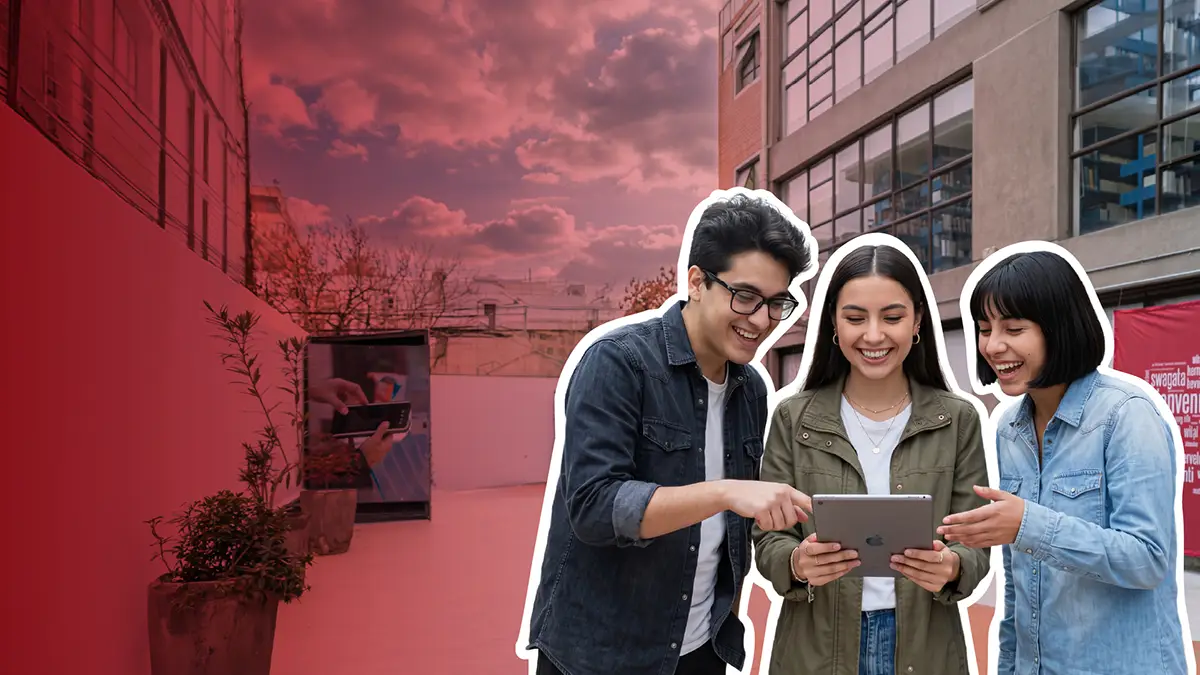 Three friends stand outdoors, smiling as they look at a tablet, with one person pointing at the screen and collaborating.